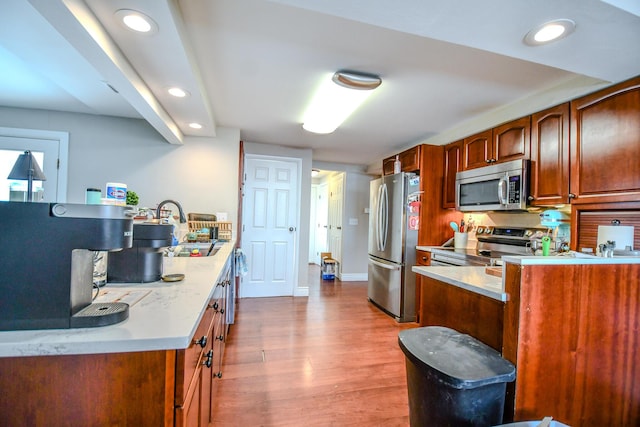 kitchen featuring brown cabinetry, appliances with stainless steel finishes, wood finished floors, a sink, and recessed lighting