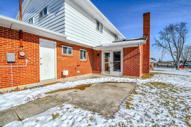 snow covered property with a chimney and brick siding