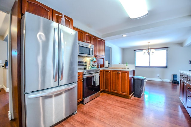 kitchen featuring stainless steel appliances, a peninsula, light countertops, light wood finished floors, and pendant lighting