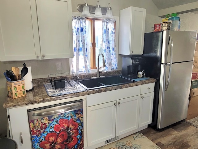 kitchen featuring appliances with stainless steel finishes, dark countertops, wood finished floors, a sink, and white cabinetry