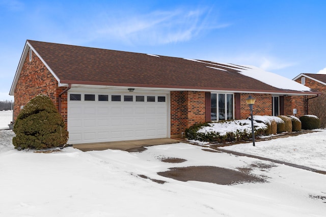 single story home featuring a garage, a shingled roof, and brick siding