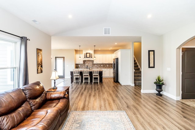 living room with visible vents, stairs, arched walkways, lofted ceiling, and light wood-style floors