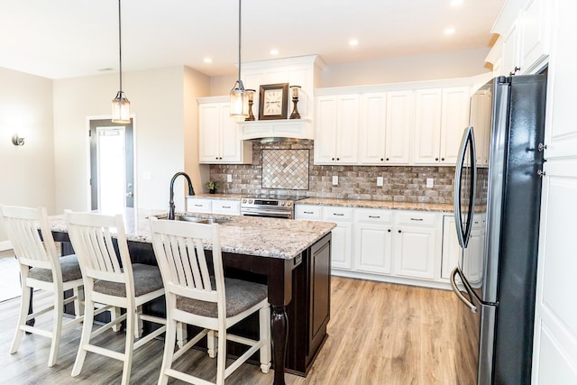 kitchen with a sink, tasteful backsplash, appliances with stainless steel finishes, light wood-type flooring, and white cabinets