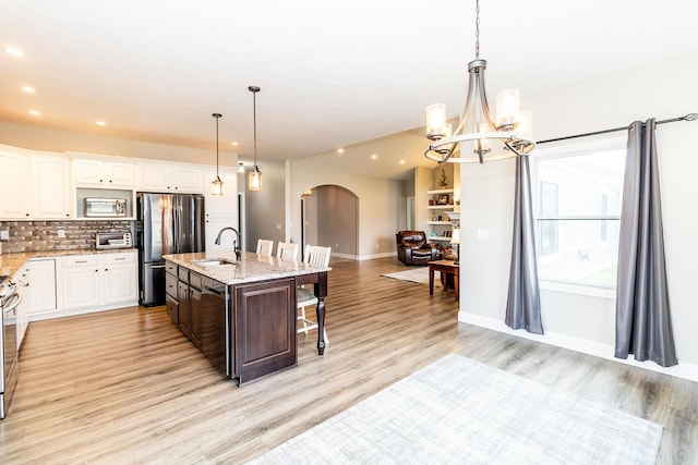 kitchen featuring decorative backsplash, a kitchen bar, stainless steel appliances, arched walkways, and a notable chandelier
