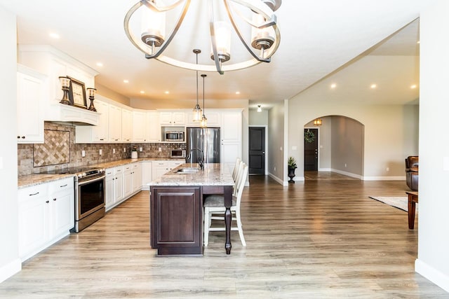kitchen featuring backsplash, white cabinets, stainless steel appliances, and arched walkways