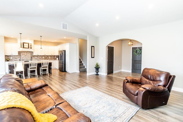 living room with light wood-style flooring, visible vents, stairs, arched walkways, and lofted ceiling