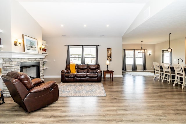 living room featuring a stone fireplace, baseboards, a notable chandelier, and wood finished floors