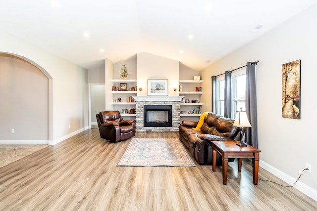 living room featuring arched walkways, a fireplace, lofted ceiling, baseboards, and light wood-style floors