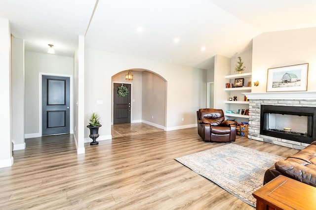 living room featuring lofted ceiling, light wood-type flooring, baseboards, arched walkways, and a fireplace