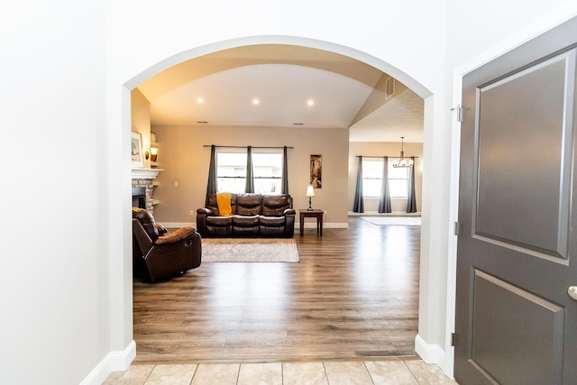 living area featuring baseboards, a wealth of natural light, light wood-style floors, and a stone fireplace