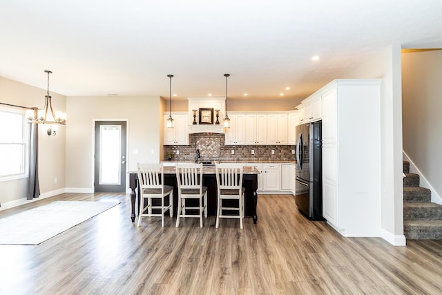 kitchen featuring an island with sink, backsplash, freestanding refrigerator, light wood-style flooring, and white cabinets