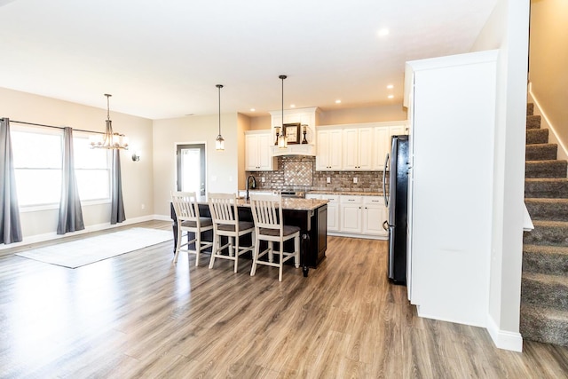 kitchen with tasteful backsplash, a breakfast bar, light wood finished floors, a kitchen island with sink, and appliances with stainless steel finishes