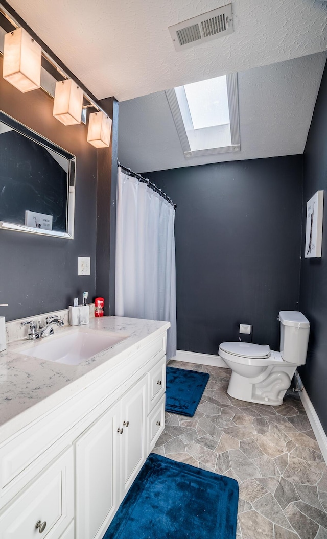 bathroom with visible vents, toilet, a skylight, stone finish floor, and a textured ceiling