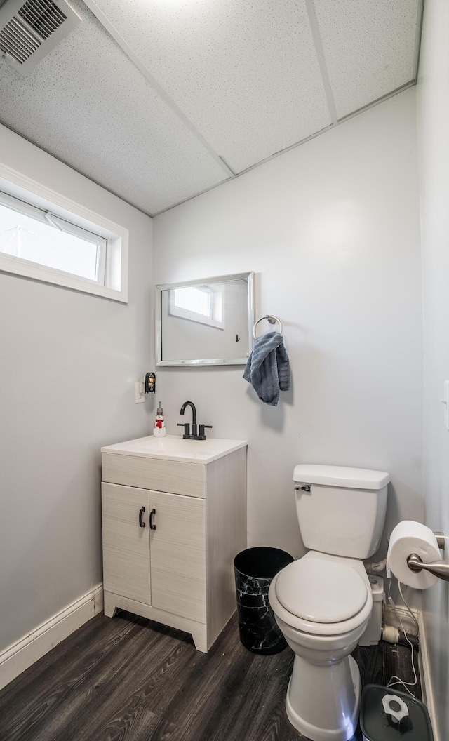 half bathroom with visible vents, toilet, a drop ceiling, wood finished floors, and baseboards