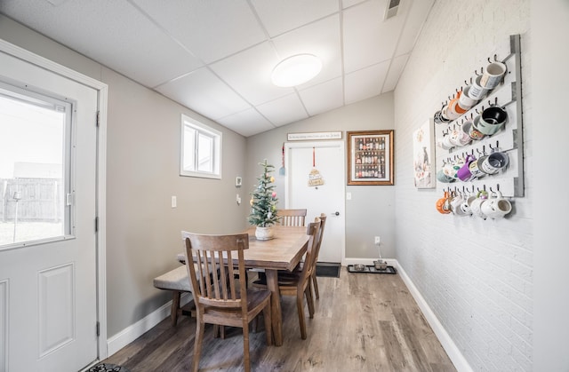 dining space featuring visible vents, a paneled ceiling, baseboards, and wood finished floors