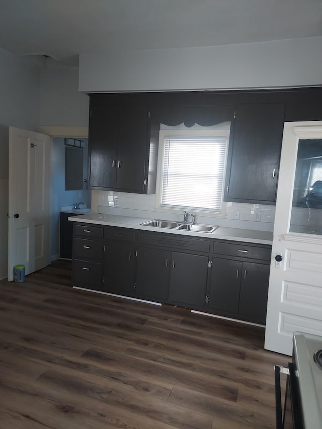 kitchen featuring decorative backsplash, stove, dark wood-style floors, and a sink