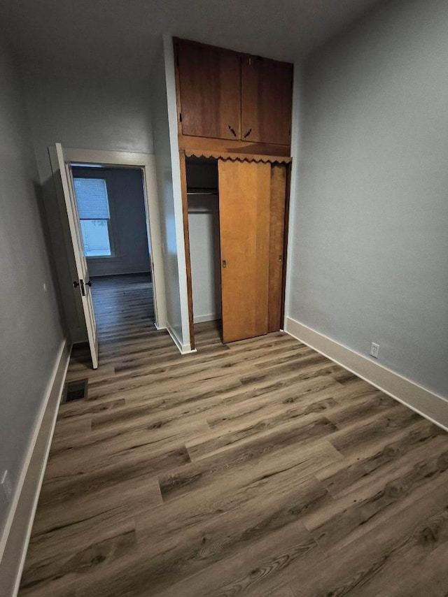 unfurnished bedroom featuring dark wood-style floors, visible vents, a closet, and baseboards