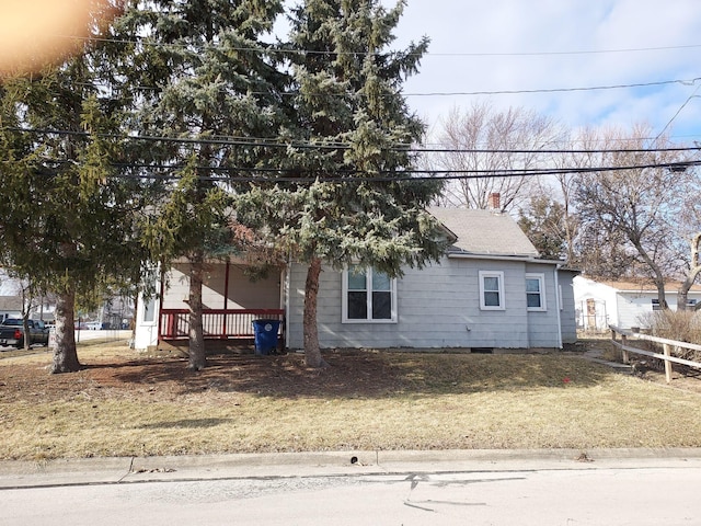 view of front facade with a front yard, covered porch, roof with shingles, and crawl space