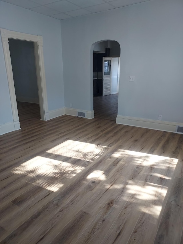 unfurnished room with visible vents, arched walkways, baseboards, and wood finished floors