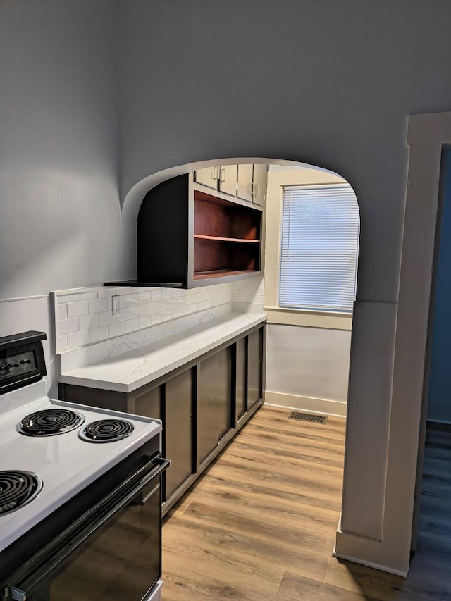 kitchen with light wood finished floors, tasteful backsplash, light countertops, electric range, and open shelves