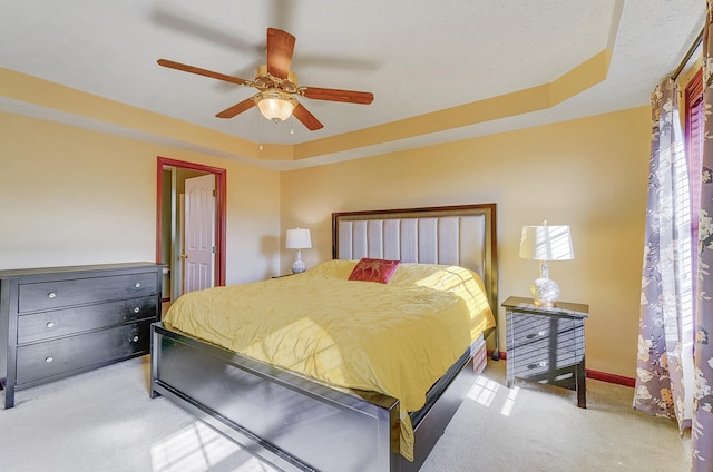 bedroom featuring light carpet, a tray ceiling, baseboards, and ceiling fan