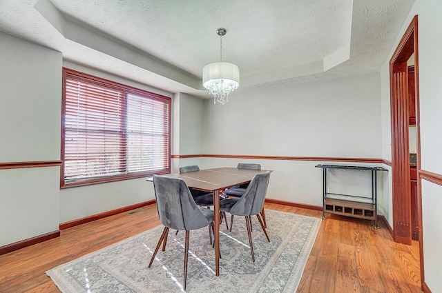 dining area featuring a chandelier, a tray ceiling, a textured ceiling, and wood finished floors