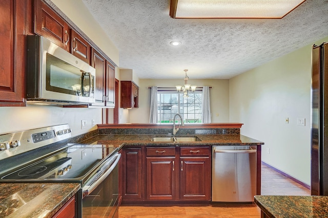kitchen with an inviting chandelier, a peninsula, appliances with stainless steel finishes, light wood finished floors, and a sink