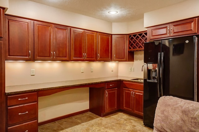 kitchen with black fridge, built in desk, a sink, a textured ceiling, and dark brown cabinets