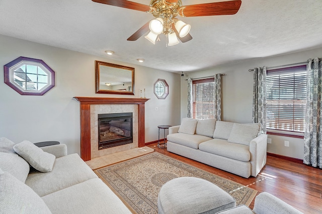living area with ceiling fan, a healthy amount of sunlight, wood finished floors, and a tiled fireplace