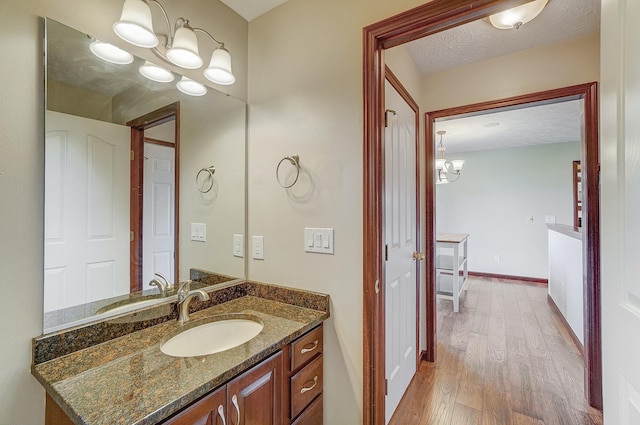 bathroom featuring an inviting chandelier, a textured ceiling, vanity, wood finished floors, and baseboards