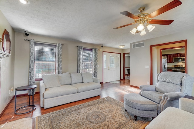 living area featuring light wood-style floors, ceiling fan, visible vents, and a textured ceiling