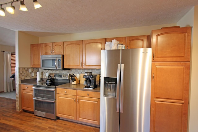609 Lambert Dr, Piqua, OH 45356 - kitchen with wood finished floors, appliances with stainless steel finishes, a textured ceiling, dark countertops, and decorative backsplash