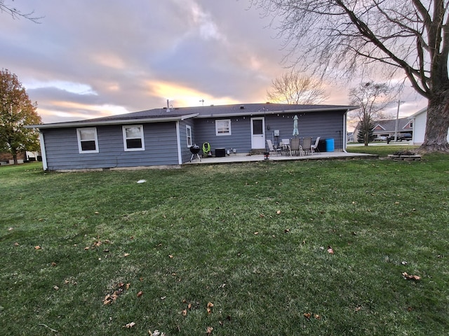 back house at dusk featuring a patio area and a lawn