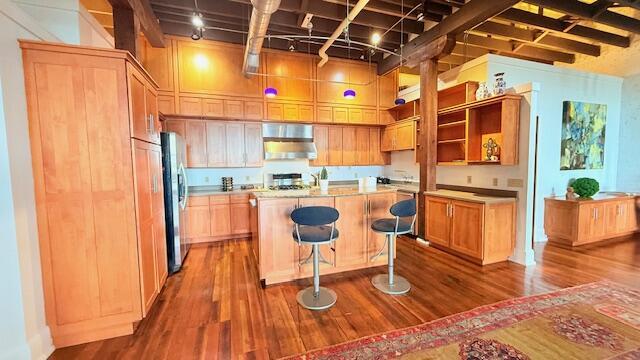 kitchen with stainless steel fridge with ice dispenser, dark wood-style floors, a kitchen island, light countertops, and a breakfast bar