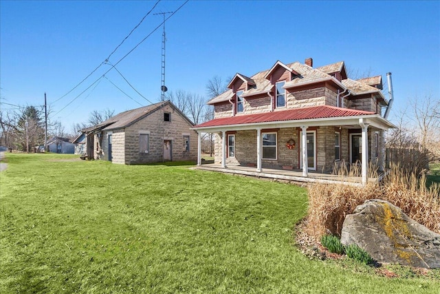view of front of property featuring metal roof, stone siding, a front yard, a porch, and a chimney