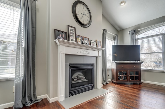 living room featuring a tile fireplace, lofted ceiling, baseboards, and wood finished floors