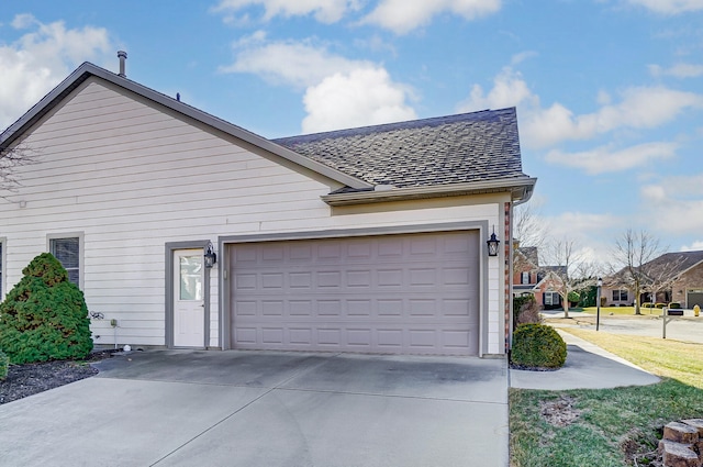 view of side of home featuring a garage, concrete driveway, and roof with shingles