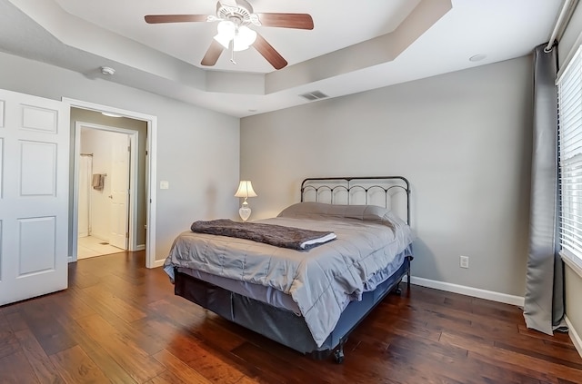 bedroom with baseboards, visible vents, a raised ceiling, and wood finished floors