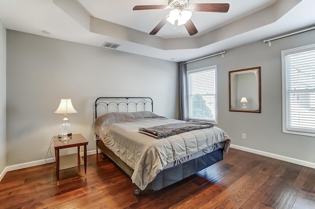 bedroom with a raised ceiling, visible vents, a ceiling fan, wood finished floors, and baseboards