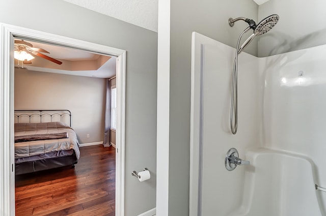 bathroom featuring a shower, a tray ceiling, ceiling fan, wood finished floors, and baseboards