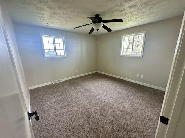 spare room with ceiling fan, a wealth of natural light, a textured ceiling, and visible vents