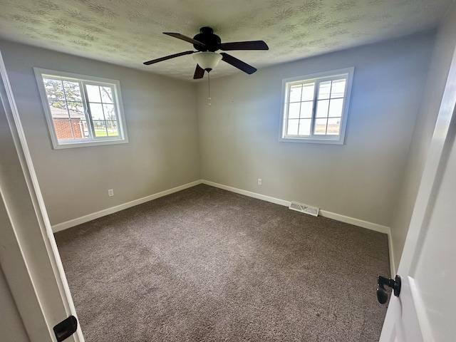 unfurnished room with dark carpet, visible vents, a ceiling fan, and a healthy amount of sunlight