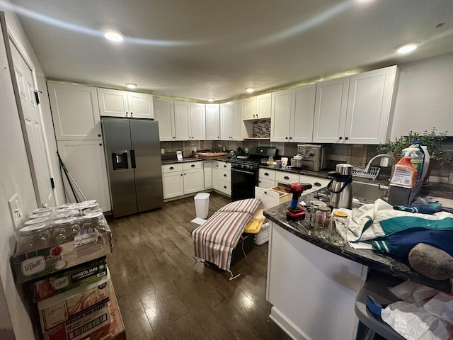 kitchen featuring black range with gas cooktop, dark countertops, stainless steel fridge, white cabinets, and dark wood-type flooring