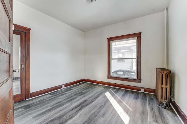 empty room featuring radiator heating unit, baseboards, and wood finished floors