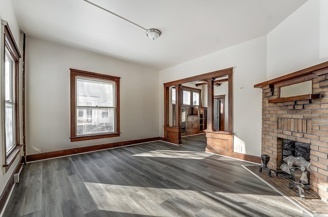 unfurnished living room with a brick fireplace, wood finished floors, and baseboards