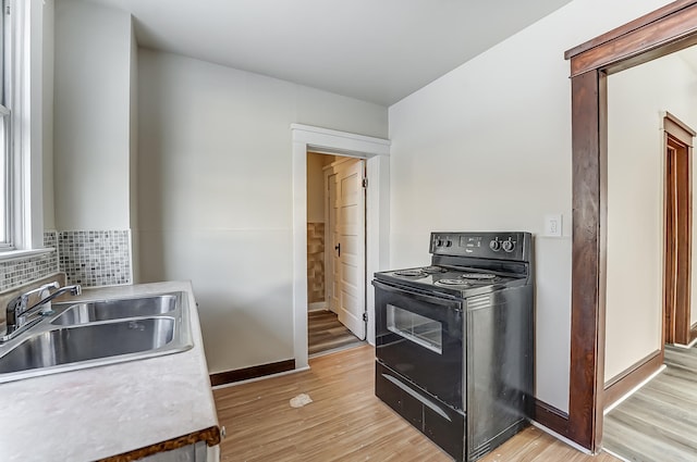 kitchen with black electric range, light wood finished floors, a sink, and decorative backsplash