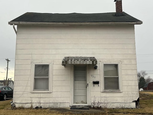 view of front facade with roof with shingles and a chimney