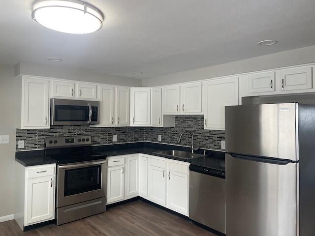 kitchen featuring appliances with stainless steel finishes, sink, white cabinets, dark wood-type flooring, and decorative backsplash