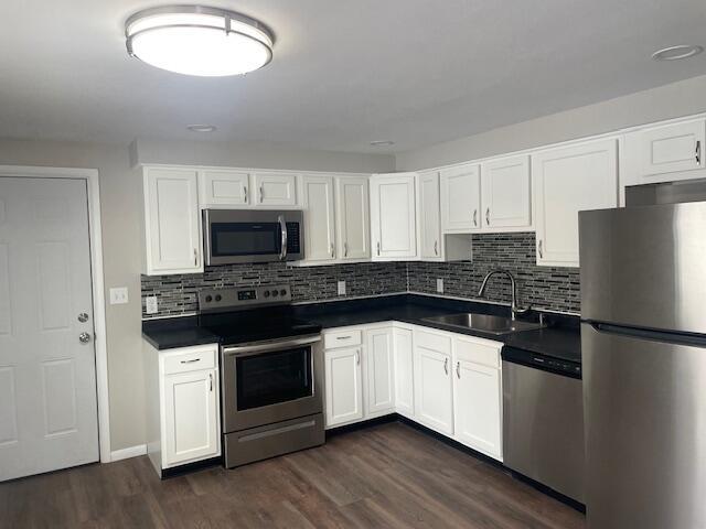 kitchen with white cabinets, appliances with stainless steel finishes, dark hardwood / wood-style flooring, decorative backsplash, and sink