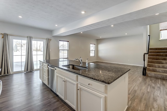 kitchen with dishwasher, white cabinetry, sink, dark stone countertops, and a kitchen island with sink